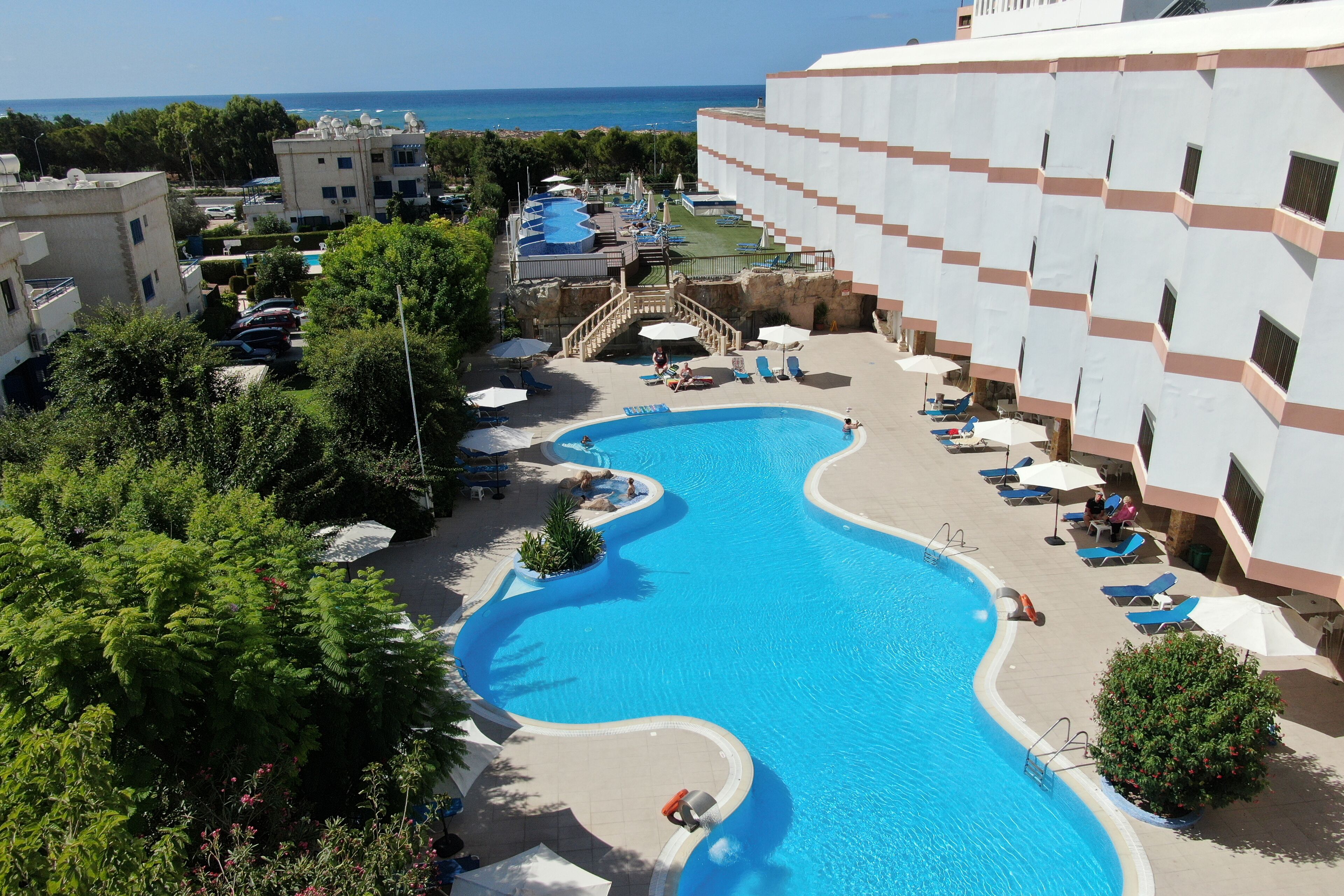 A resort with a large pool, lounge chairs, and a view of the sea.