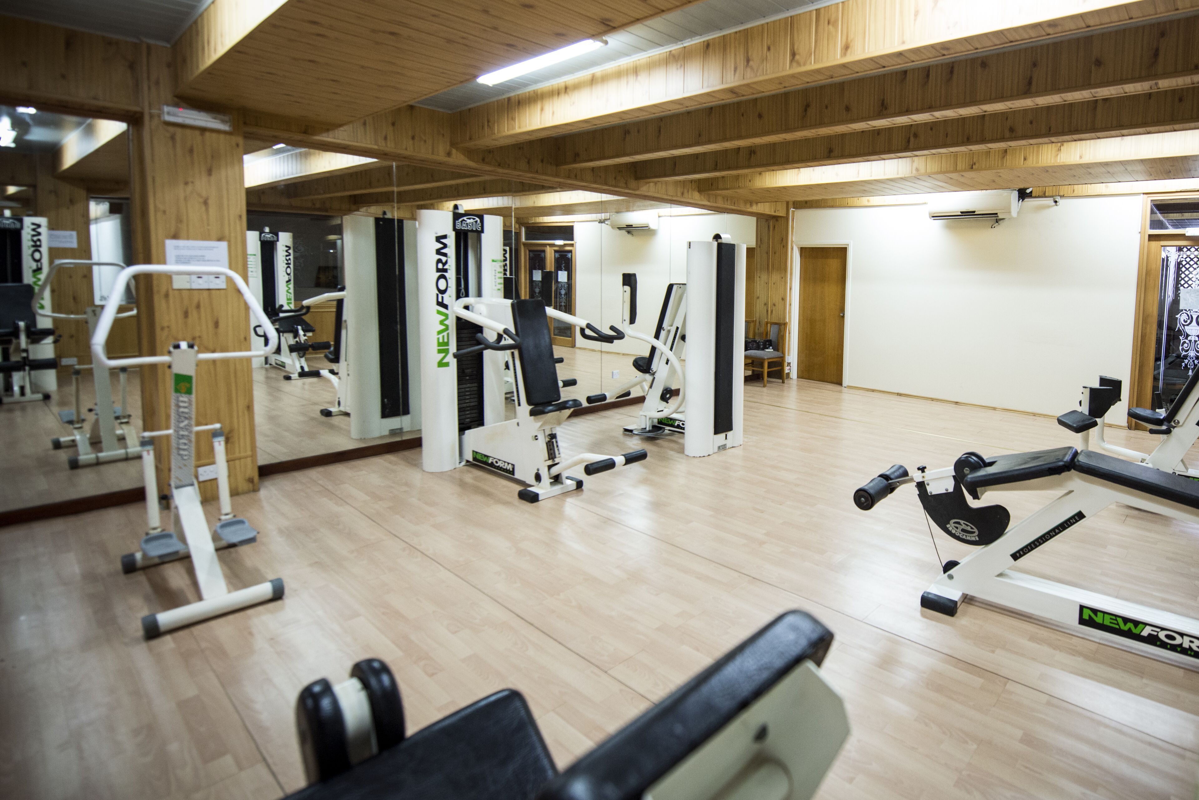 A gym with various exercise equipment, wooden floors, and a mirrored wall.