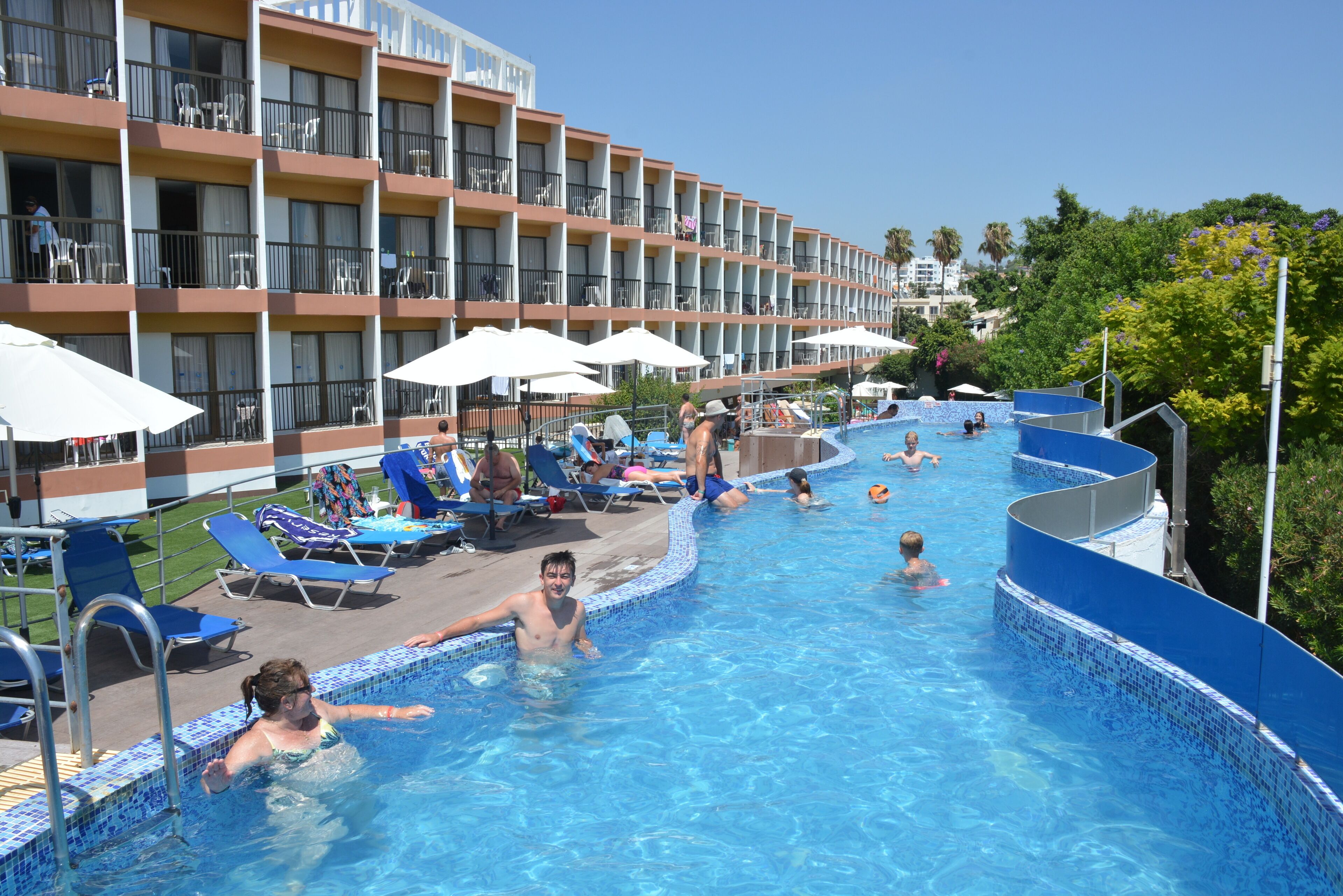 Ein Hotelpoolbereich mit mehreren Balkonebenen, Liegestühlen und Sonnenschirmen.