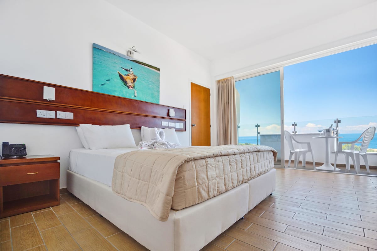 A hotel room with a bed, bedside table, and a view of the ocean through a balcony.