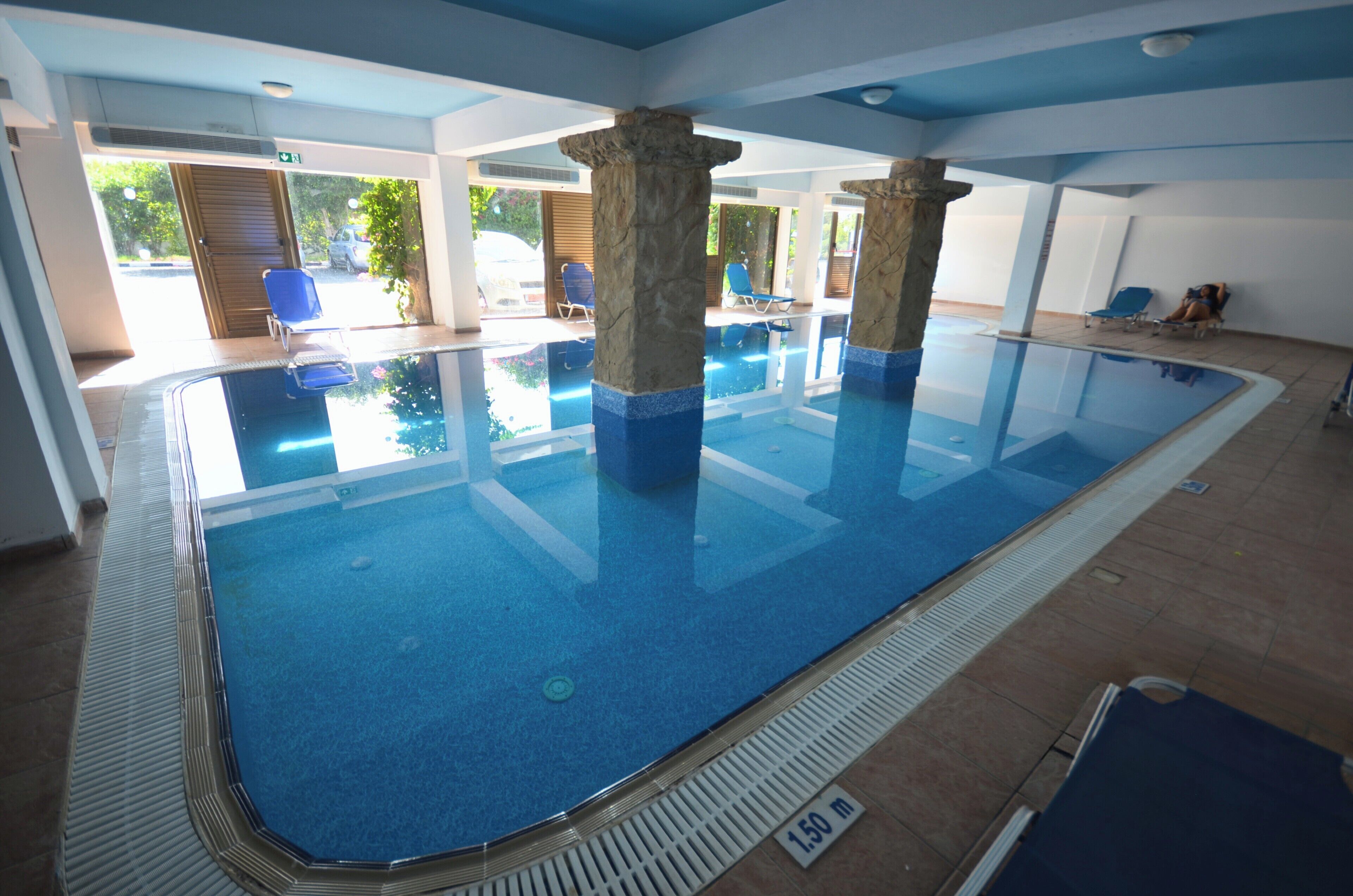Piscina interna com água cristalina, pilares de pedra e espreguiçadeiras.