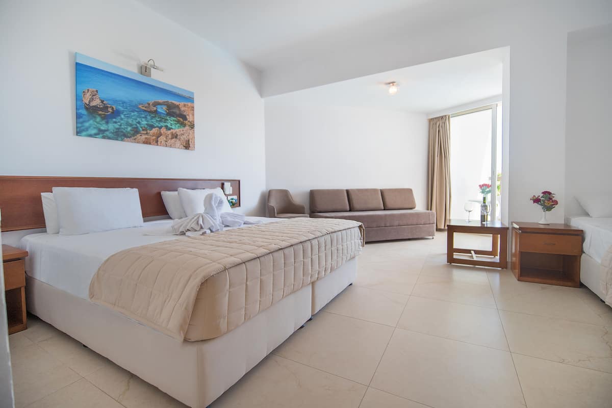 A hotel room with a large bed, a sofa, a small table with a vase of flowers, and a painting on the wall.