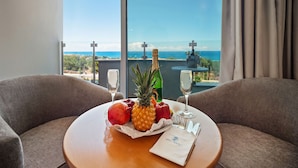 A room with a view of the ocean, a table with a bottle of champagne, fruit, and a menu. - Avlida Hotel (Paphos)
