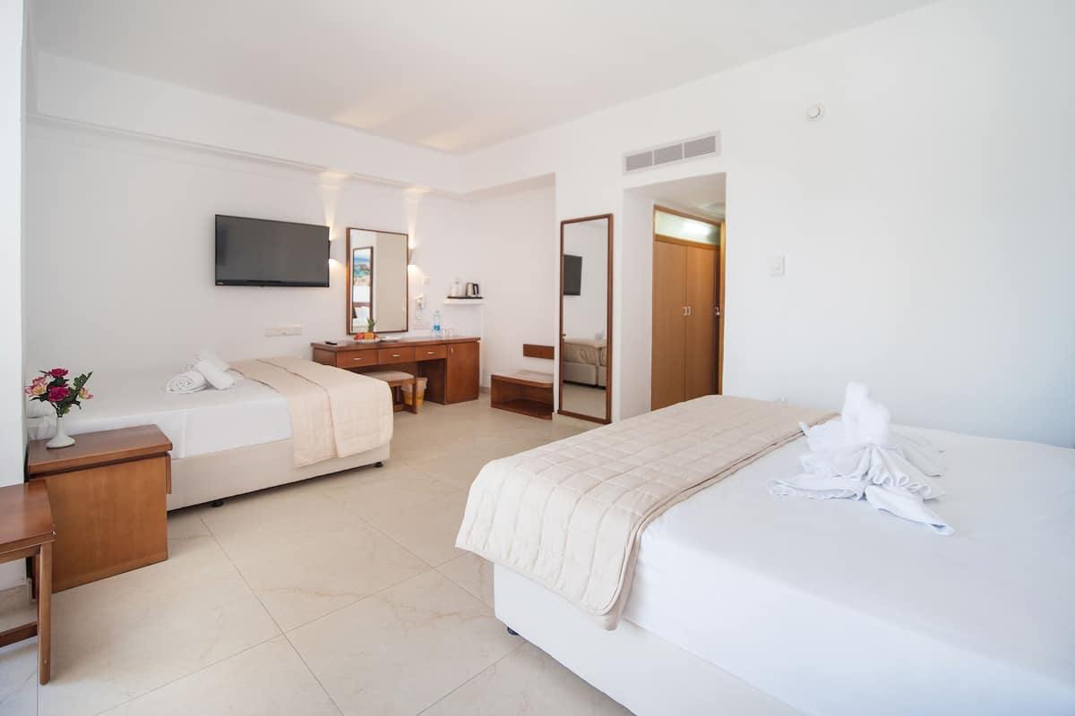 A hotel room with two beds, a desk, a mirror, a TV, and a bathroom visible through an open door.