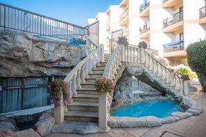 Zona de piscina con una escalera de piedra que lleva a un balcón, rodeada por un paisaje rocoso.
