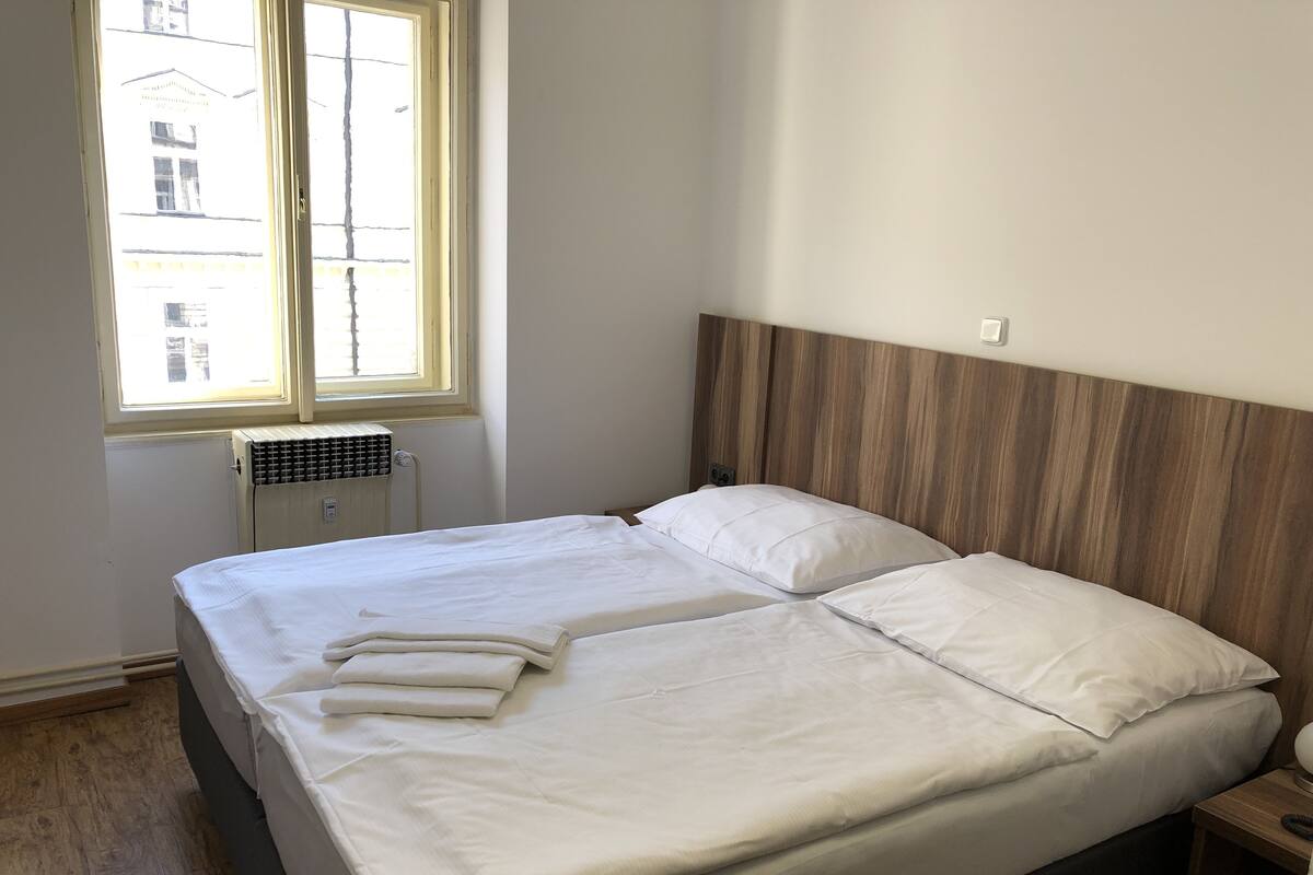Ein ordentlich bezogenes Bett mit weißen Leinen in einem Zimmer, das ein Holz-Kopfteil und ein Fenster hat.