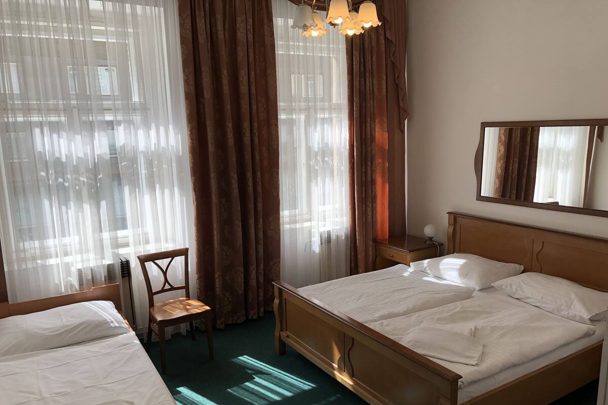 Ein Hotelzimmer mit zwei Betten, einem Sessel, einem Nachttisch mit Lampe und einem großen Spiegel an der Wand.
