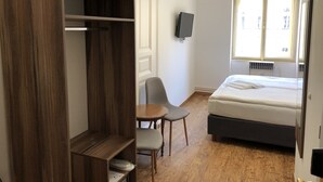 Un dormitorio con cama, armario de madera, escritorio, silla y televisor en la pared.