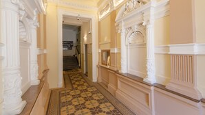 Un amplio pasillo con columnas blancas ornamentales y un piso estampado, que conduce a una escalera.