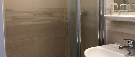Un baño con cabina de ducha de vidrio, un lavabo blanco y un espejo sobre el lavabo.