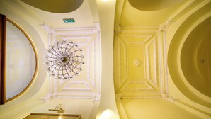 Una habitación con detalles ornamentales en el techo, una araña y una obra de arte enmarcada en la pared.