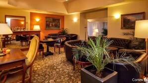 Un hall de hotel con una zona de bar, sofás de cuero, una planta grande en maceta y una alfombra estampada.