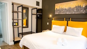 Une chambre d’hôtel avec un lit, un tableau représentant un paysage urbain, une étagère et une chaise.