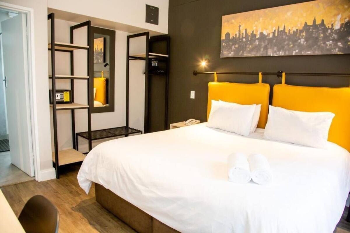 Een hotelkamer met een bed, een stadsgezicht schilderij, een wandplank en een stoel.