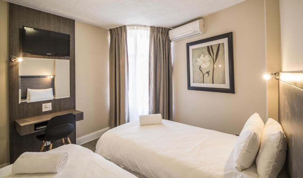 Habitación de hotel con dos camas, un escritorio, una silla, un televisor y un cuadro en la pared.