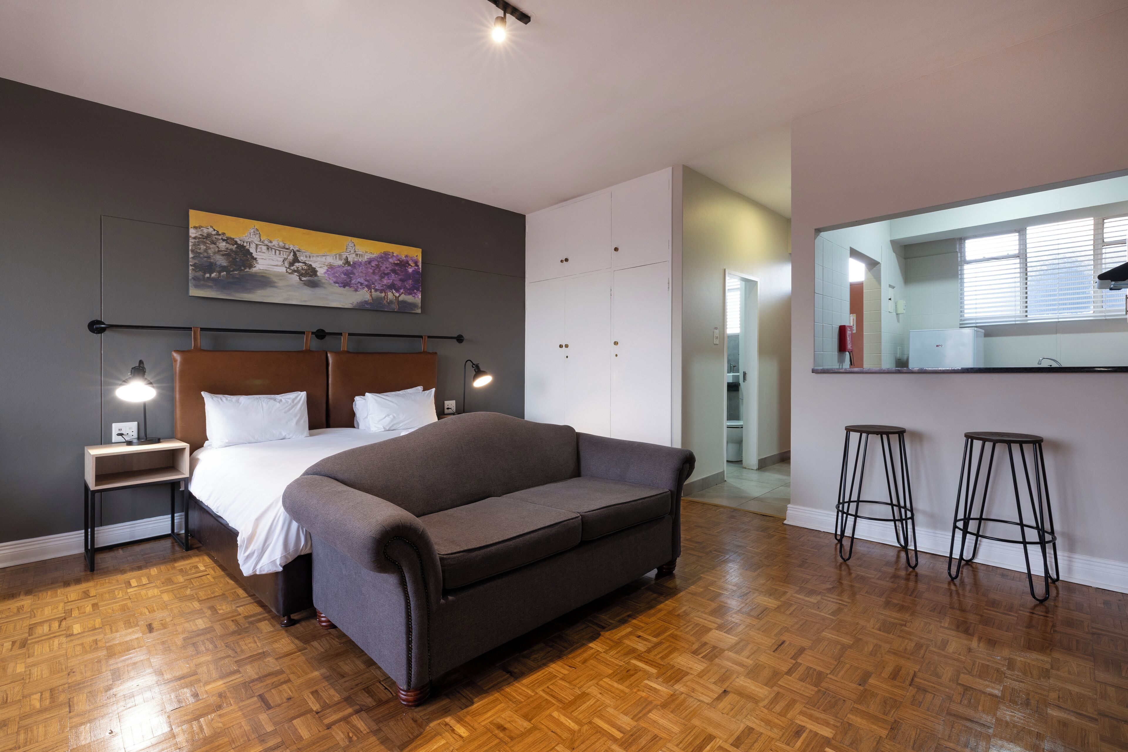 A modern bedroom with a large bed, a sofa, a desk, and a mirror.