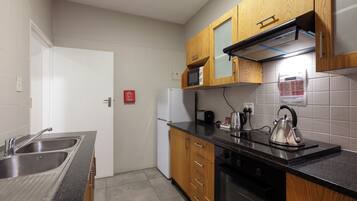 A compact kitchen with a stainless steel sink, wooden cabinets, a microwave, and a kettle.