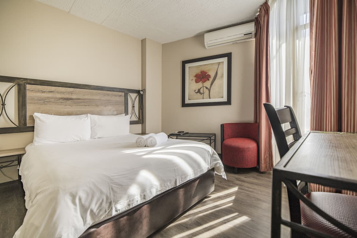 Hotelkamer met een groot bed, een klein tafeltje, een stoel, een nachtkastje en een ingelijste foto aan de muur.