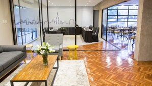 Une salle de réunion moderne avec un mur en verre, un plancher en bois, un canapé, une table basse et un fauteuil jaune qui apporte une touche de couleur.