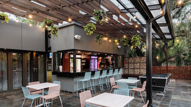 Un espace extérieur aménagé en terrasse, avec des tables et des chaises, un comptoir de bar et des plantes suspendues.