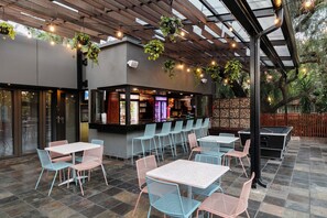 En udendørs patio med borde, stole, en bardisk og hængende planter.