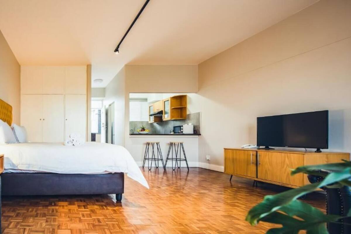 Een moderne hotelkamer met een bed, een televisie, een houten vloer, een kitchenette en een eettafel.