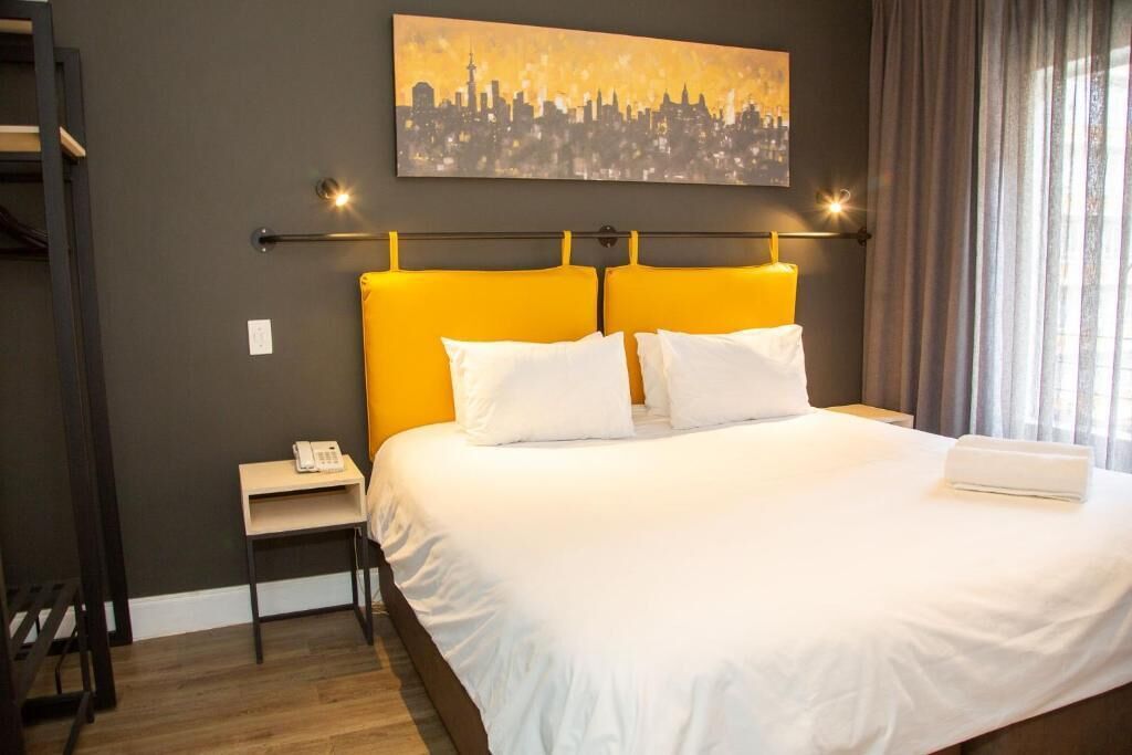 Ein Hotelzimmer mit Bett, Nachttisch, Telefon und einem Stadtbild an der Wand.