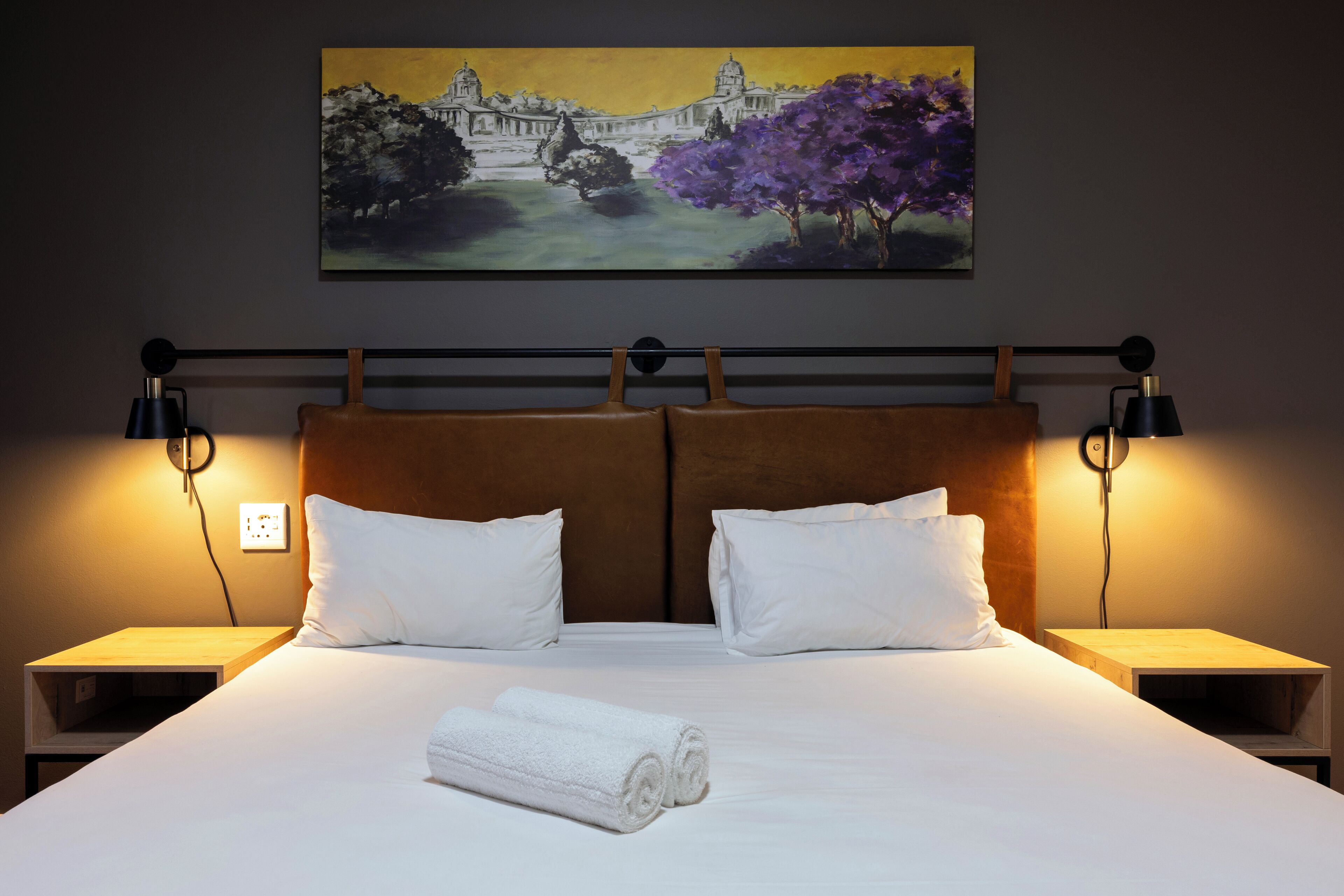 A hotel room with a large bed, two nightstands, a headboard, and a painting on the wall.
