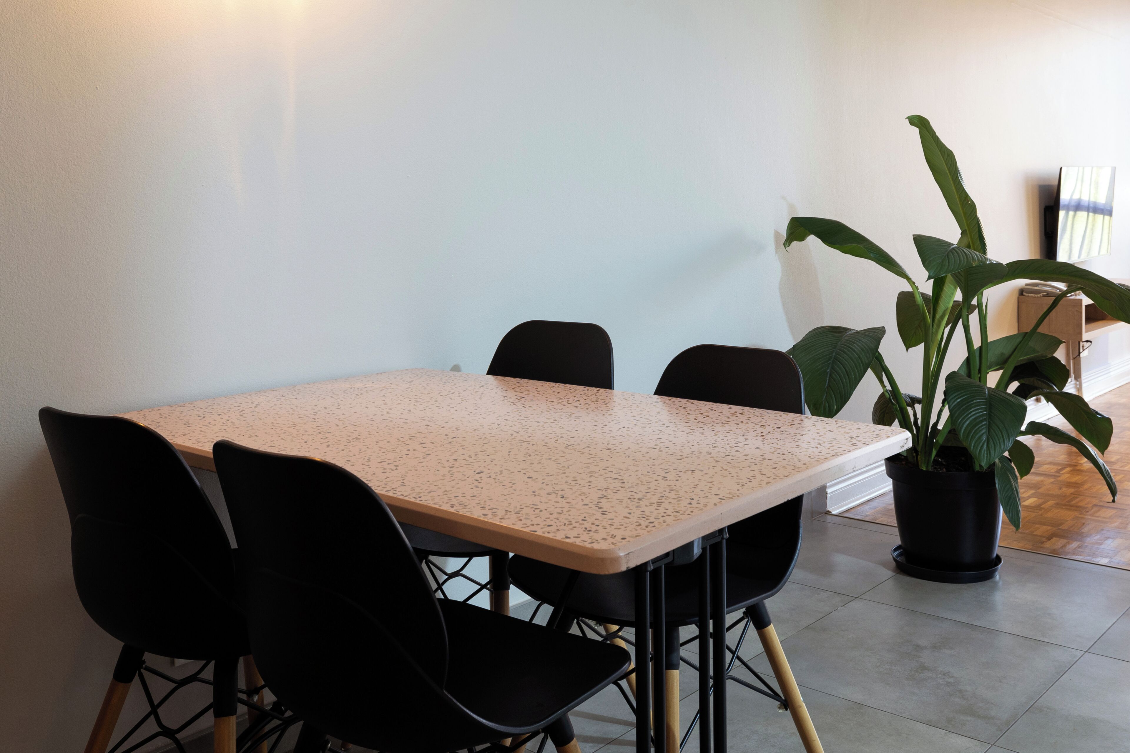 A conference table with four chairs, a potted plant, and a television on the wall.