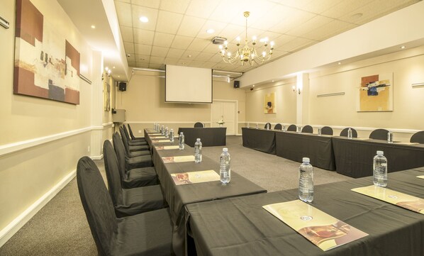 Un salón de conferencias con mesas largas, sillas y botellas de agua.