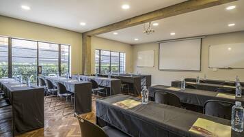 Un salón de conferencias con mesas, sillas, un proyector y una pizarra.