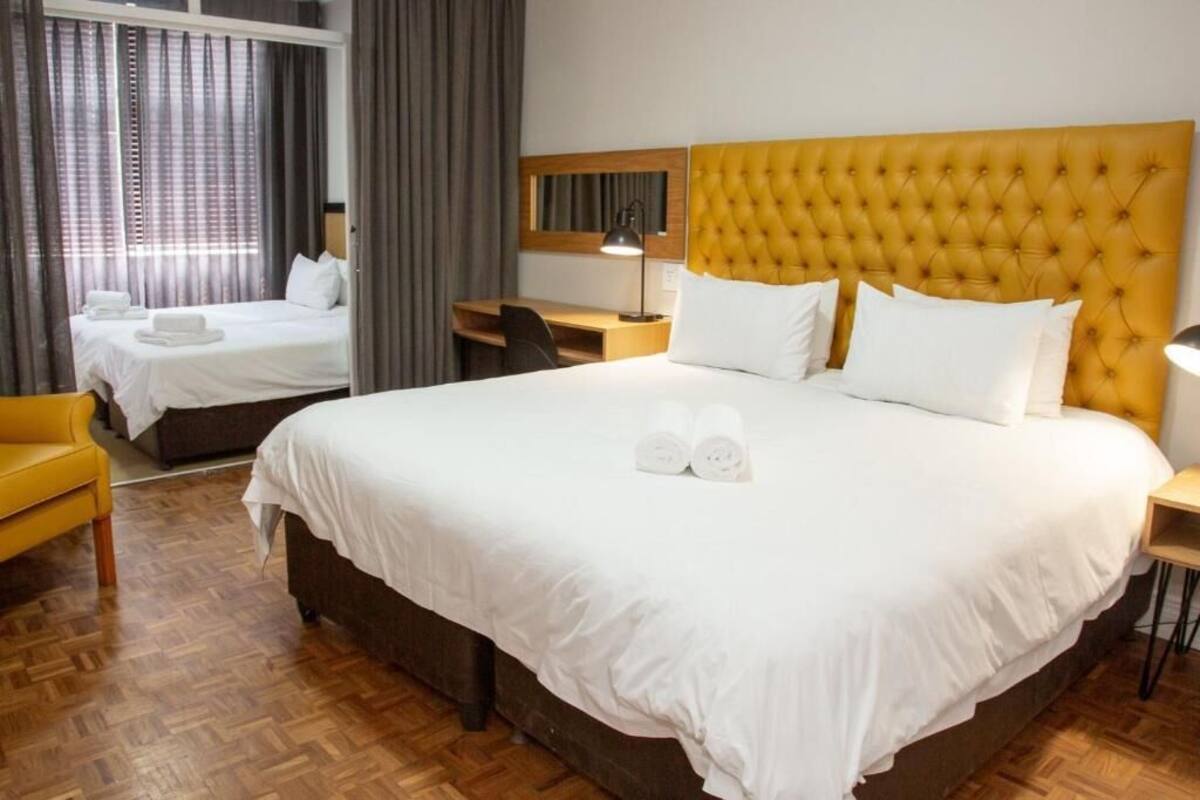 Hotelkamer met een groot bed, een kleiner bed, een bureau, een stoel en een raam met gordijnen.