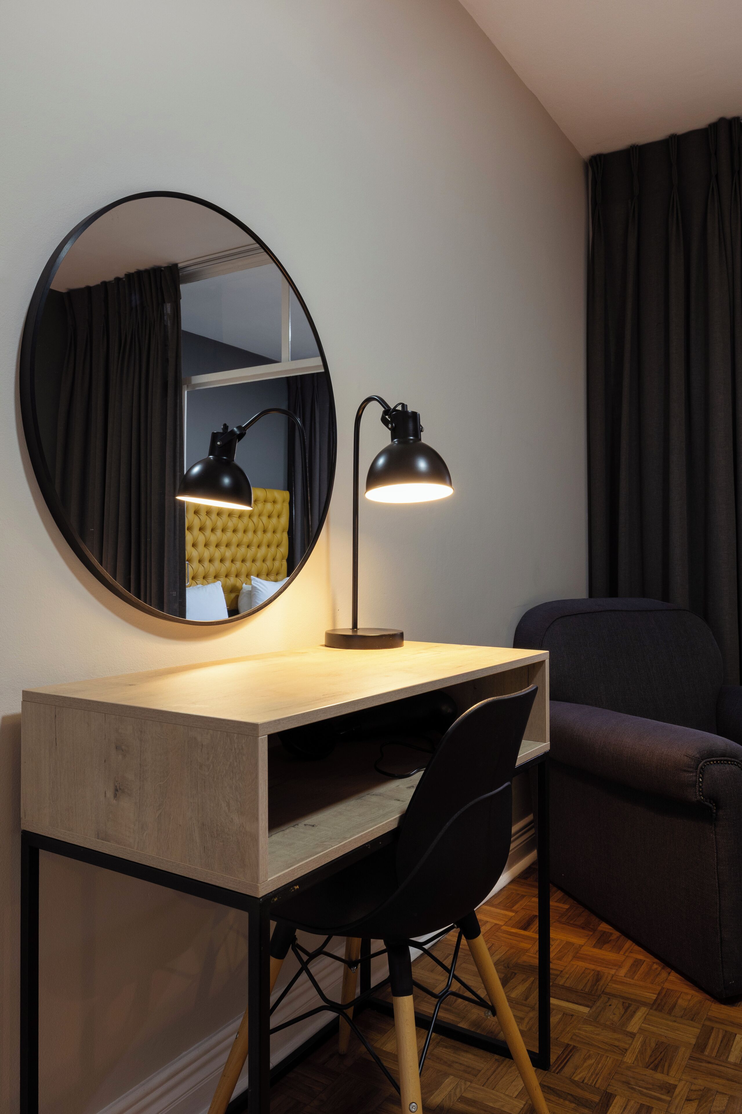 Una habitación moderna con un espejo redondo, un escritorio con una silla y un sofá.