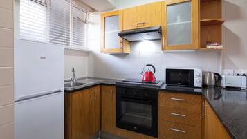 A compact kitchen with wooden cabinets, a stainless steel sink, a black oven, a microwave, and a kettle.