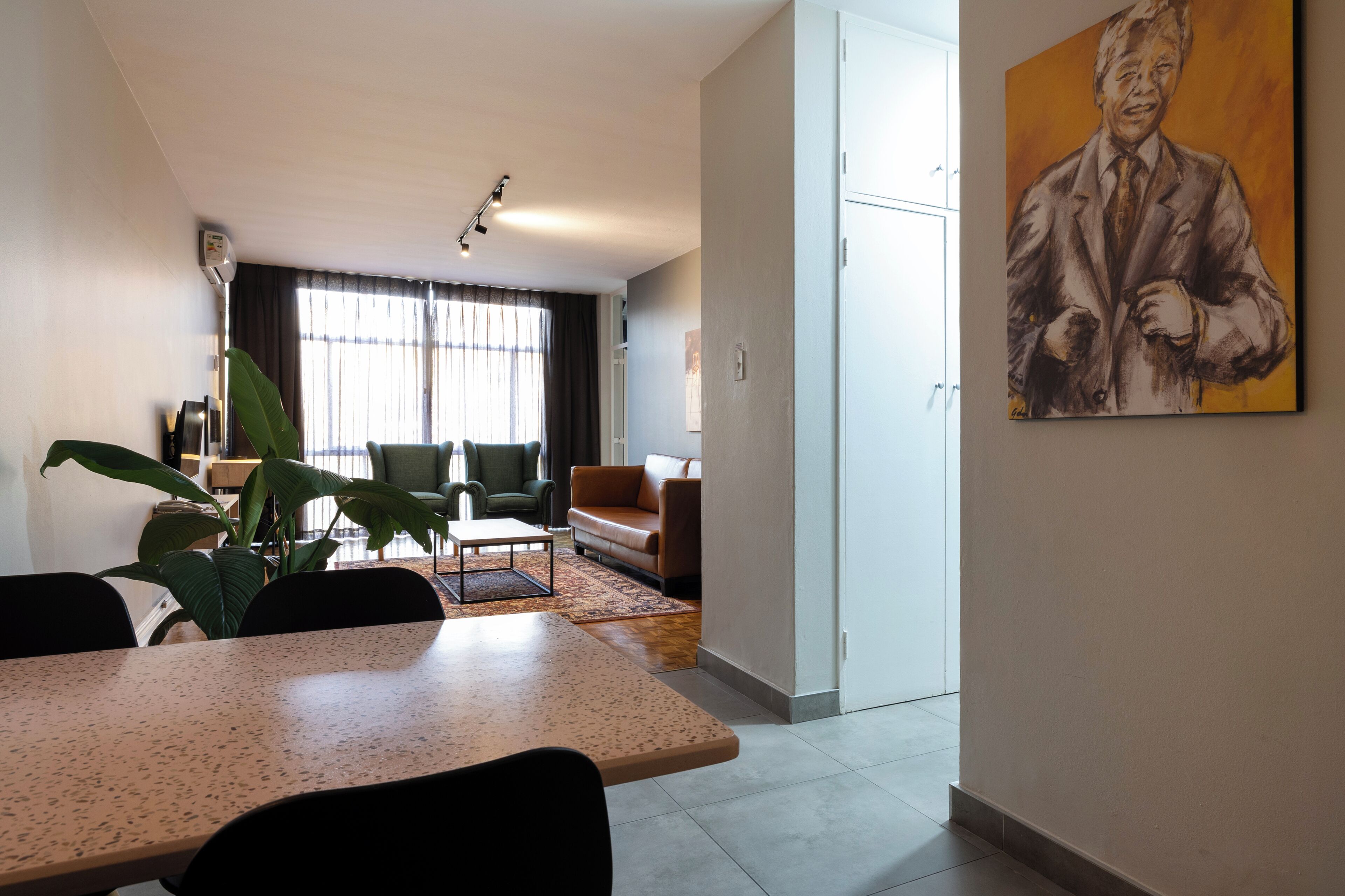 Un salon moderne comprenant un coin repas, une grande fenêtre avec des rideaux, un tableau au mur et une plante.