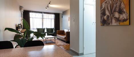 Un salon moderne comprenant un coin repas, une grande fenêtre avec des rideaux, un tableau au mur et une plante.