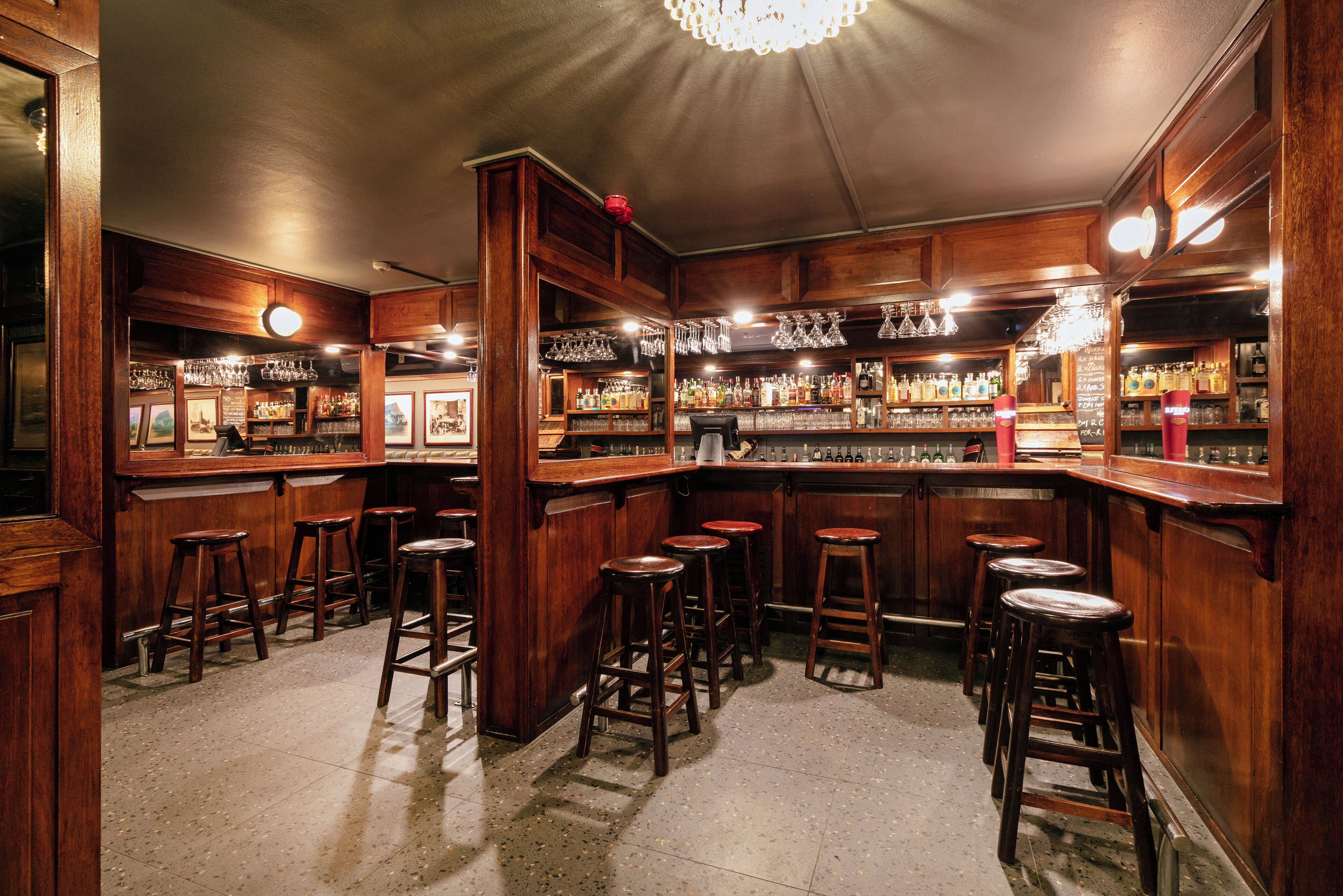 A bar with wooden decor, multiple stools, and shelves of bottles.