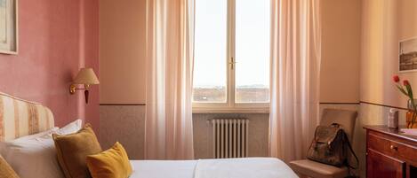 Una habitación de hotel con cama, una silla, un escritorio y ventana con cortinas.