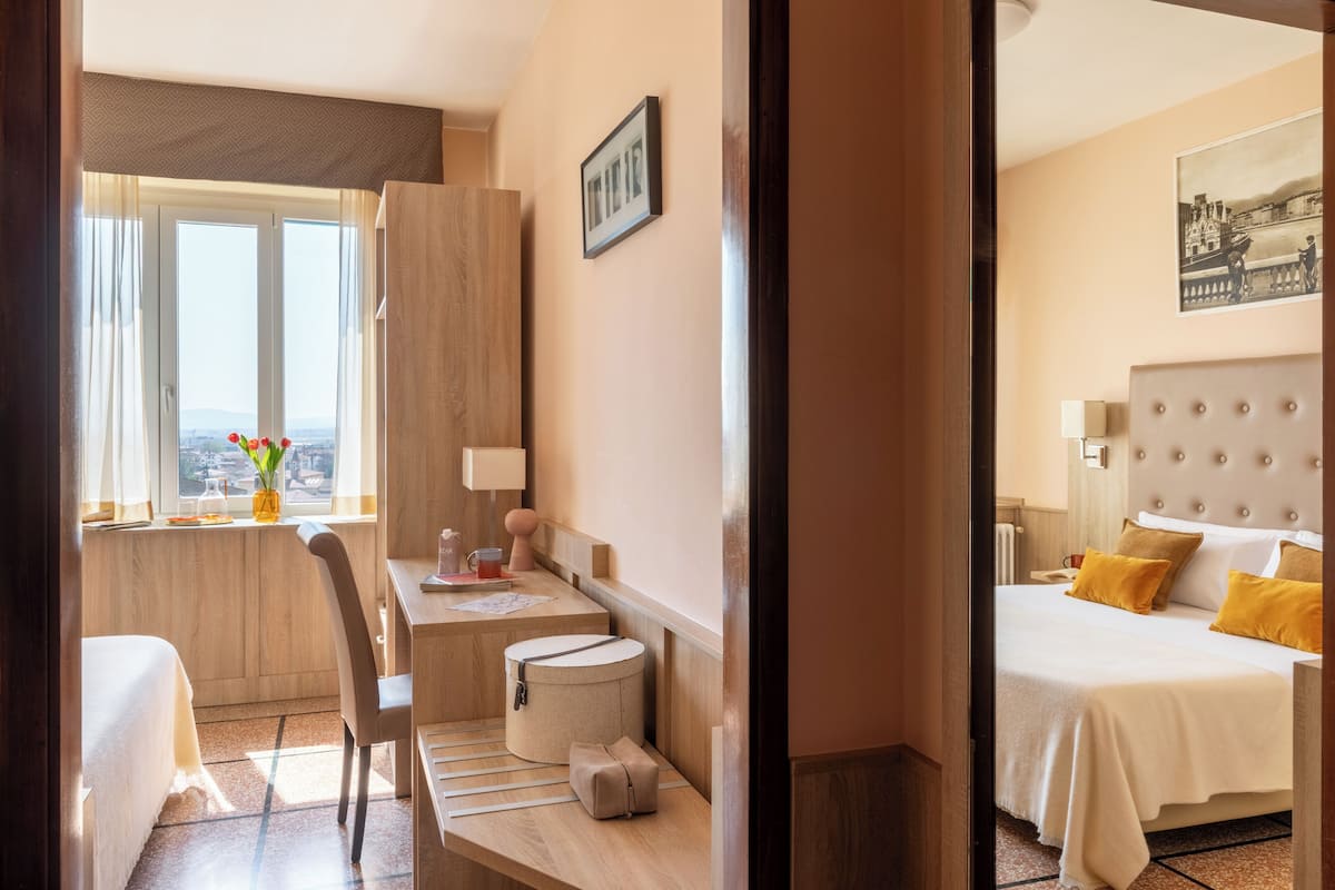Ein Hotelzimmer mit Bett, Schreibtisch, Stuhl, einem kleinen Tisch, einer Lampe und einem Fenster mit Blick.