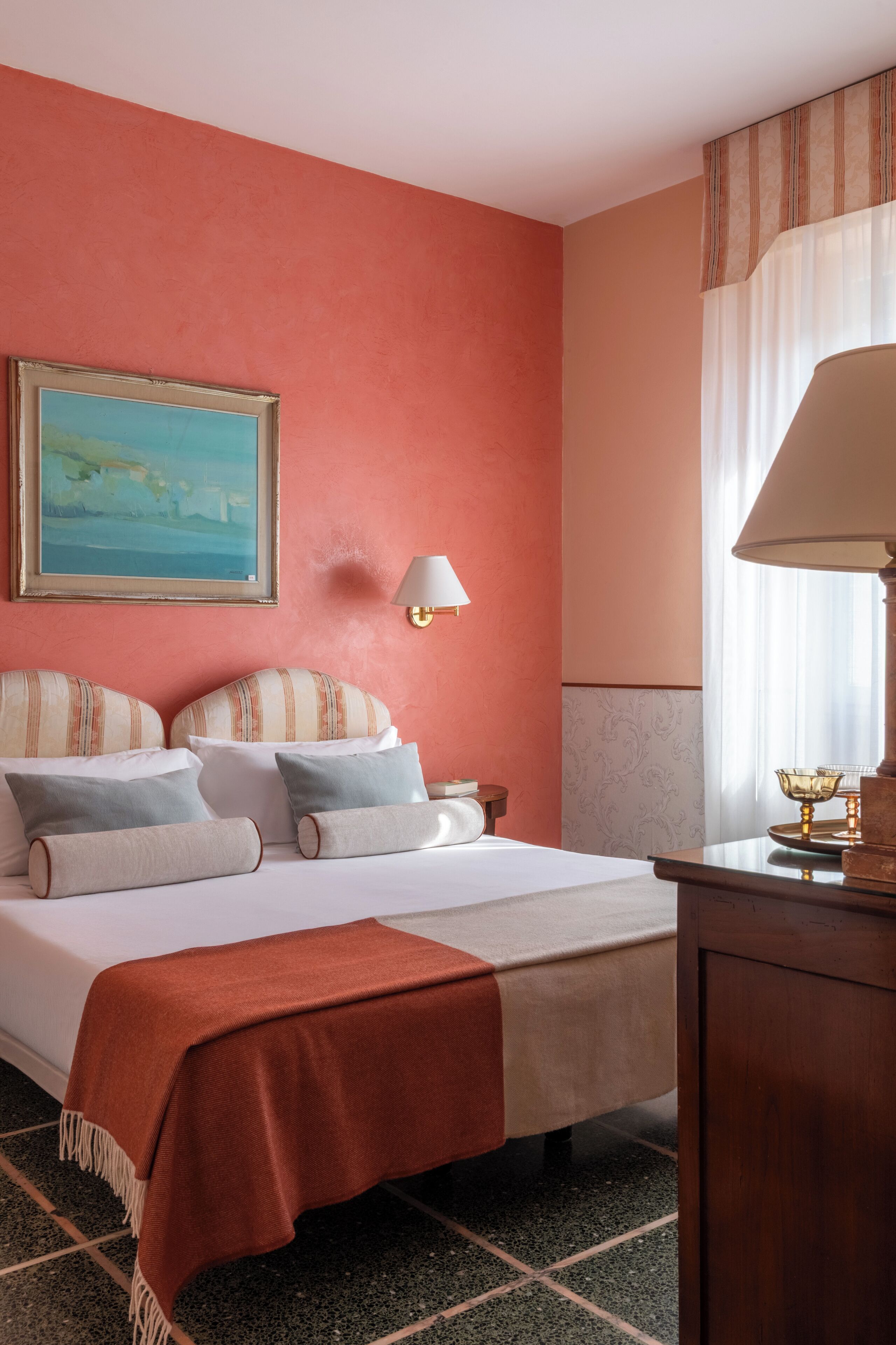 Une chambre d’hôtel avec un lit, un tableau au mur, une lampe et une fenêtre avec des rideaux.