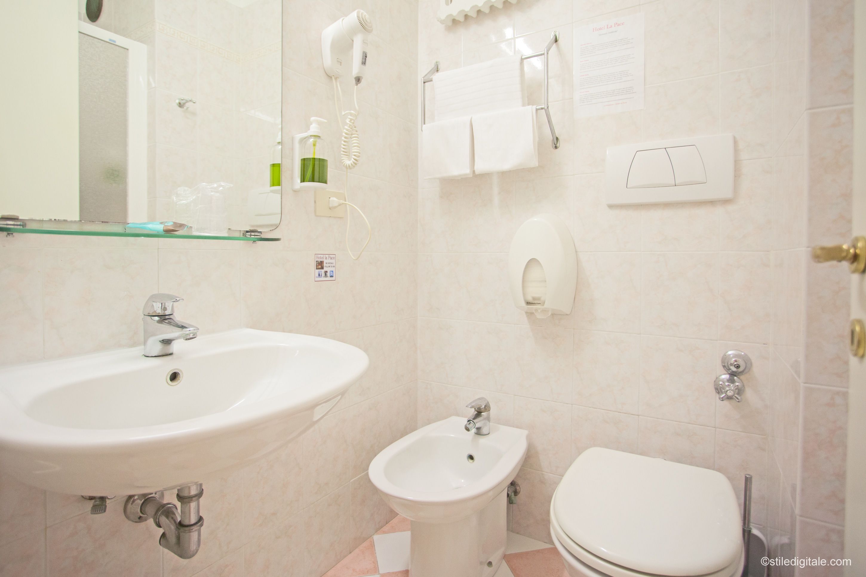 Et badeværelse med vask, bidet, toilet og en glashylde.