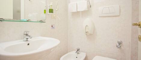 Et badeværelse med vask, bidet, toilet og en glashylde.