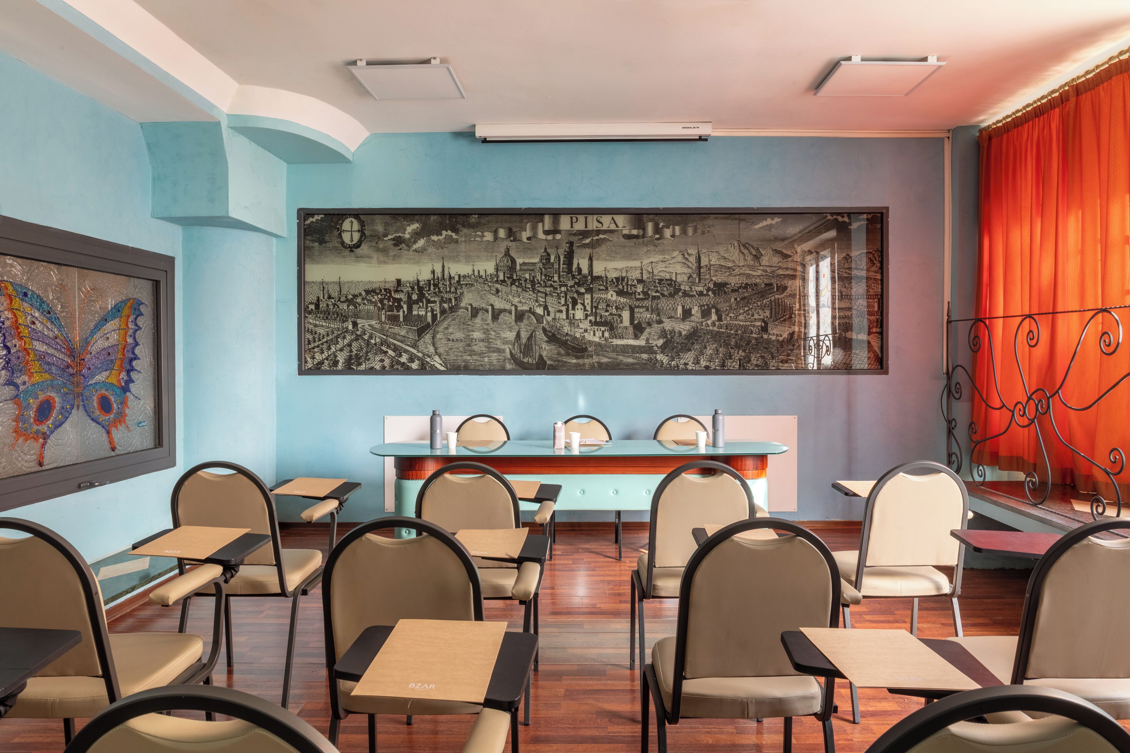 A classroom with desks, chairs, a large framed cityscape, and a butterfly painting.