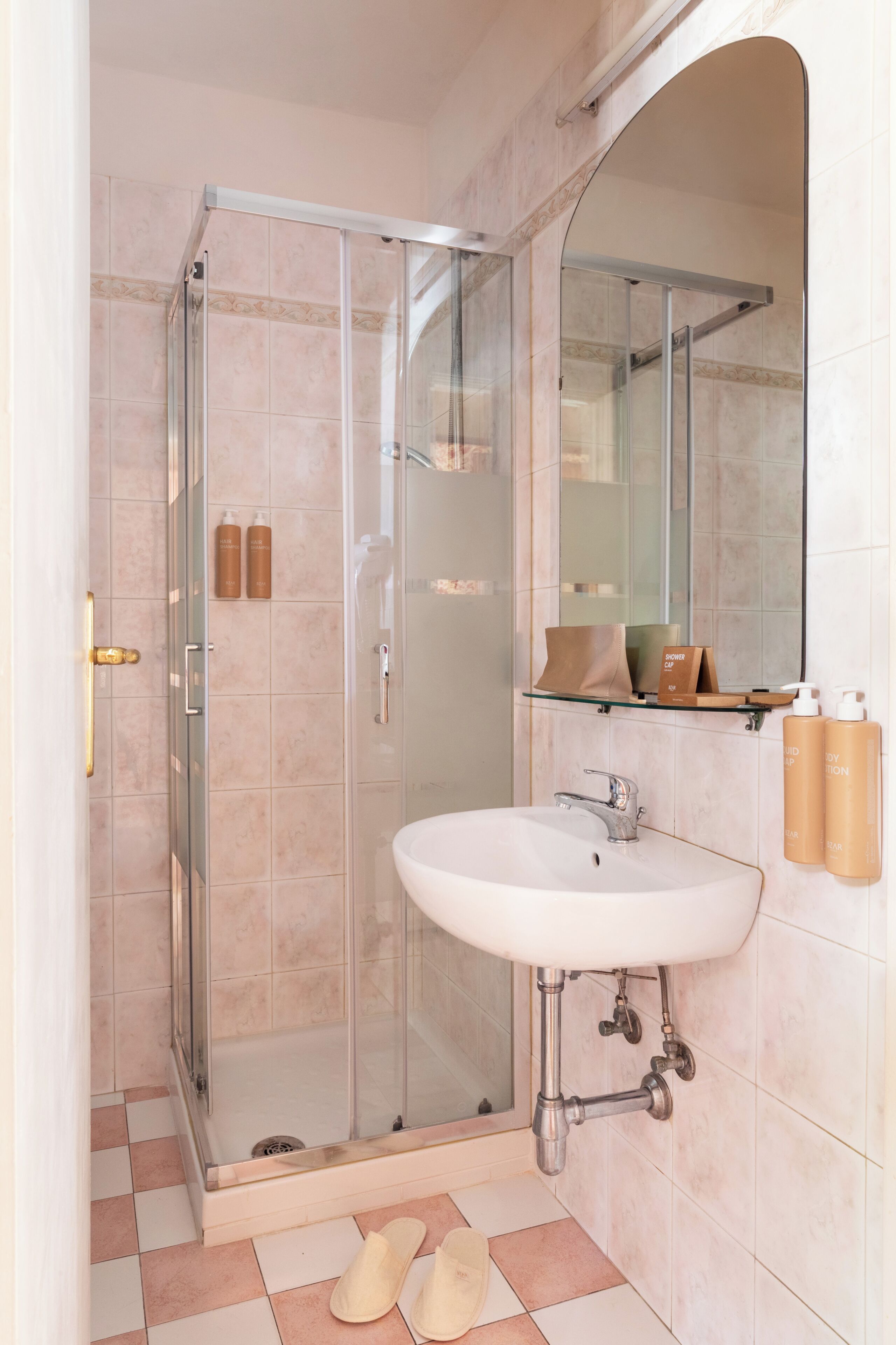 A bathroom with a glass-enclosed shower, a sink with a mirror, and toiletries on the wall.
