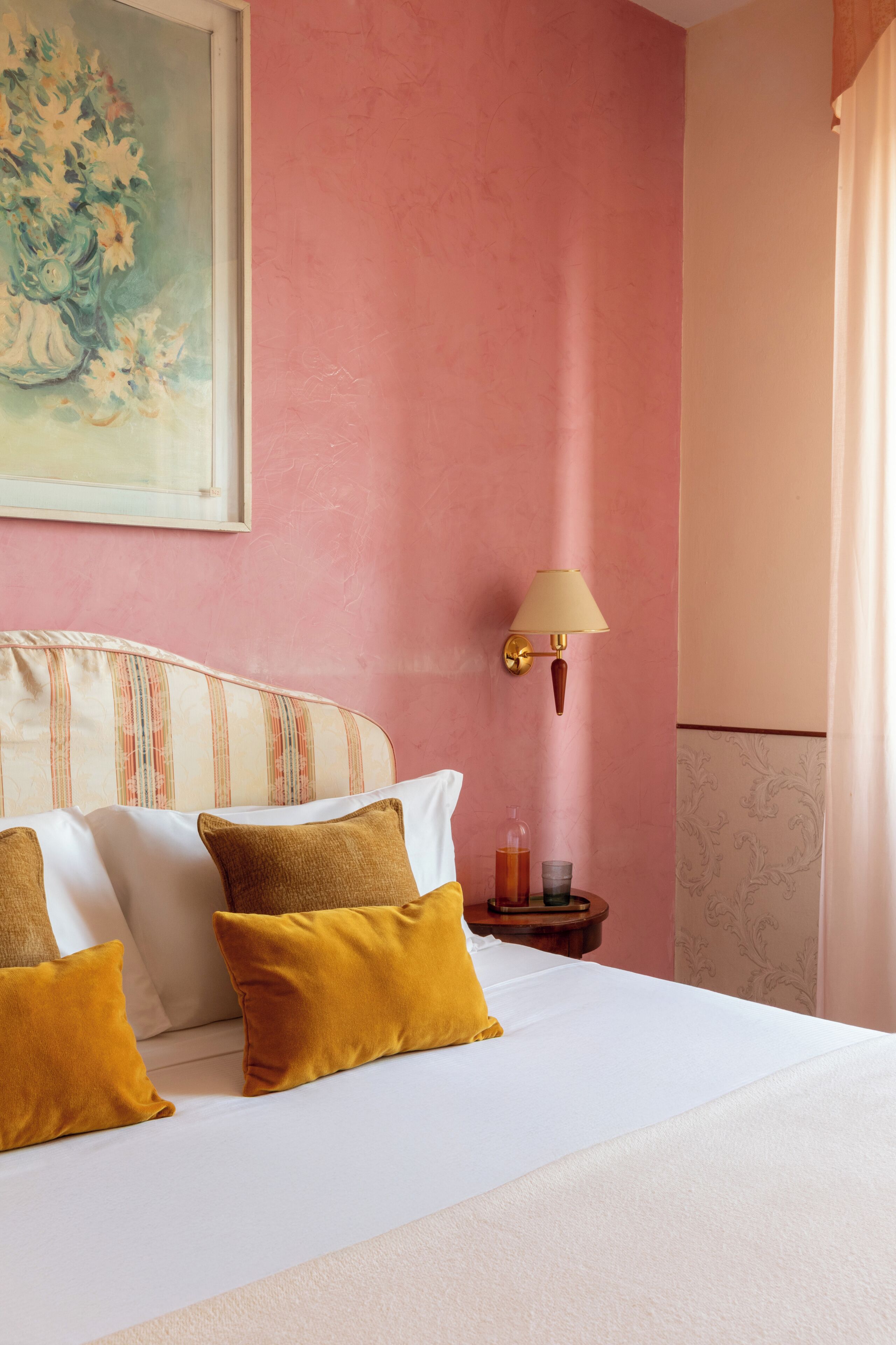 A hotel room with a bed, pillows, a nightstand, a lamp, and a painting on the wall.