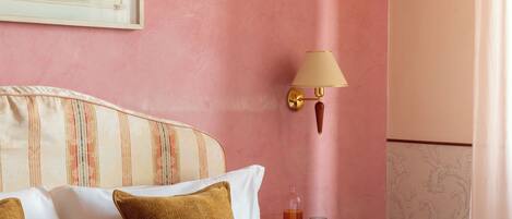 Una habitación de hotel con cama, almohadas, mesita de noche, lámpara y un cuadro en la pared.
