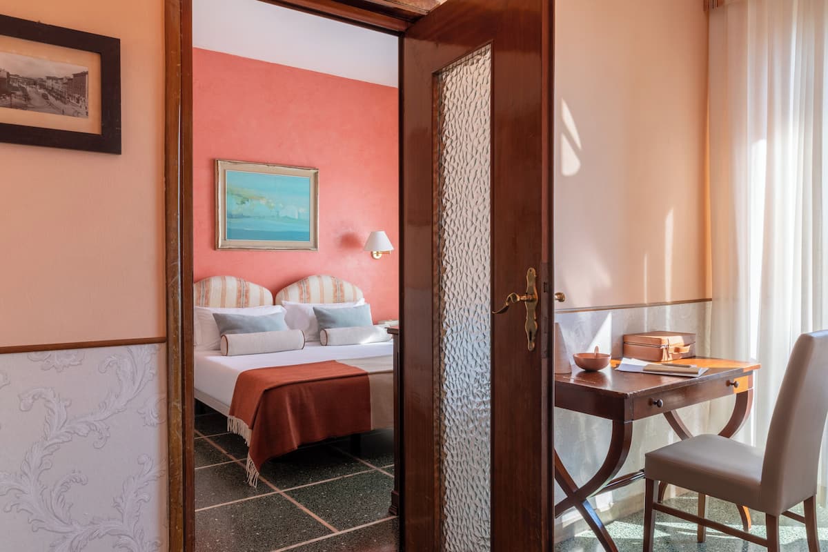 Ein Hotelzimmer mit Bett, Schreibtisch mit Stuhl, Lampe und einem Bild an der Wand.