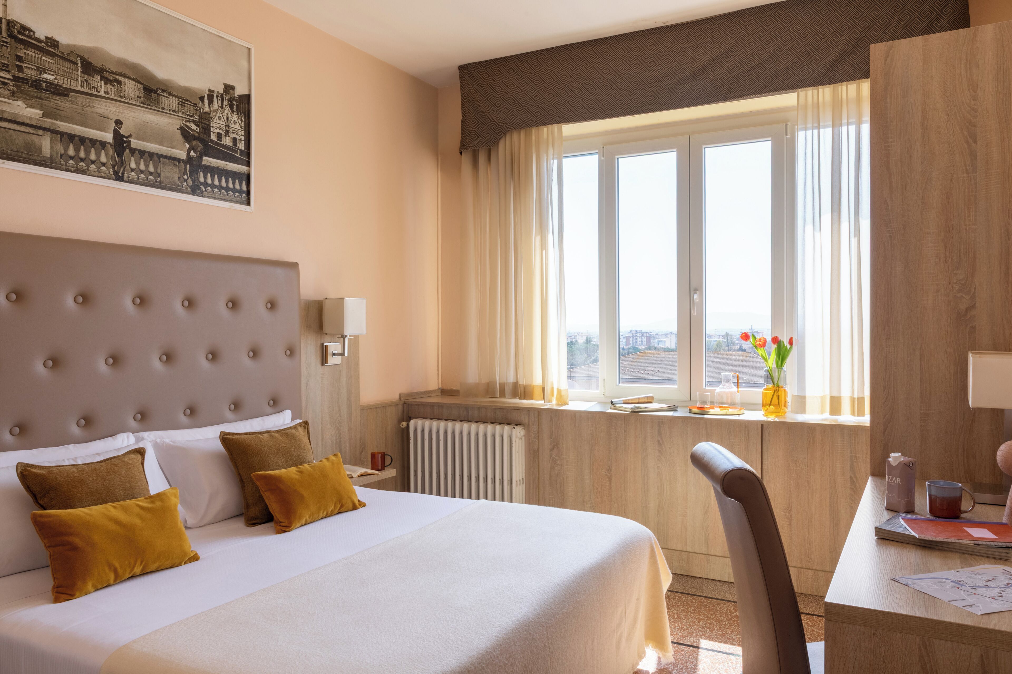 Habitación de hotel con una cama grande, un escritorio, una silla, una ventana con cortinas y un radiador.