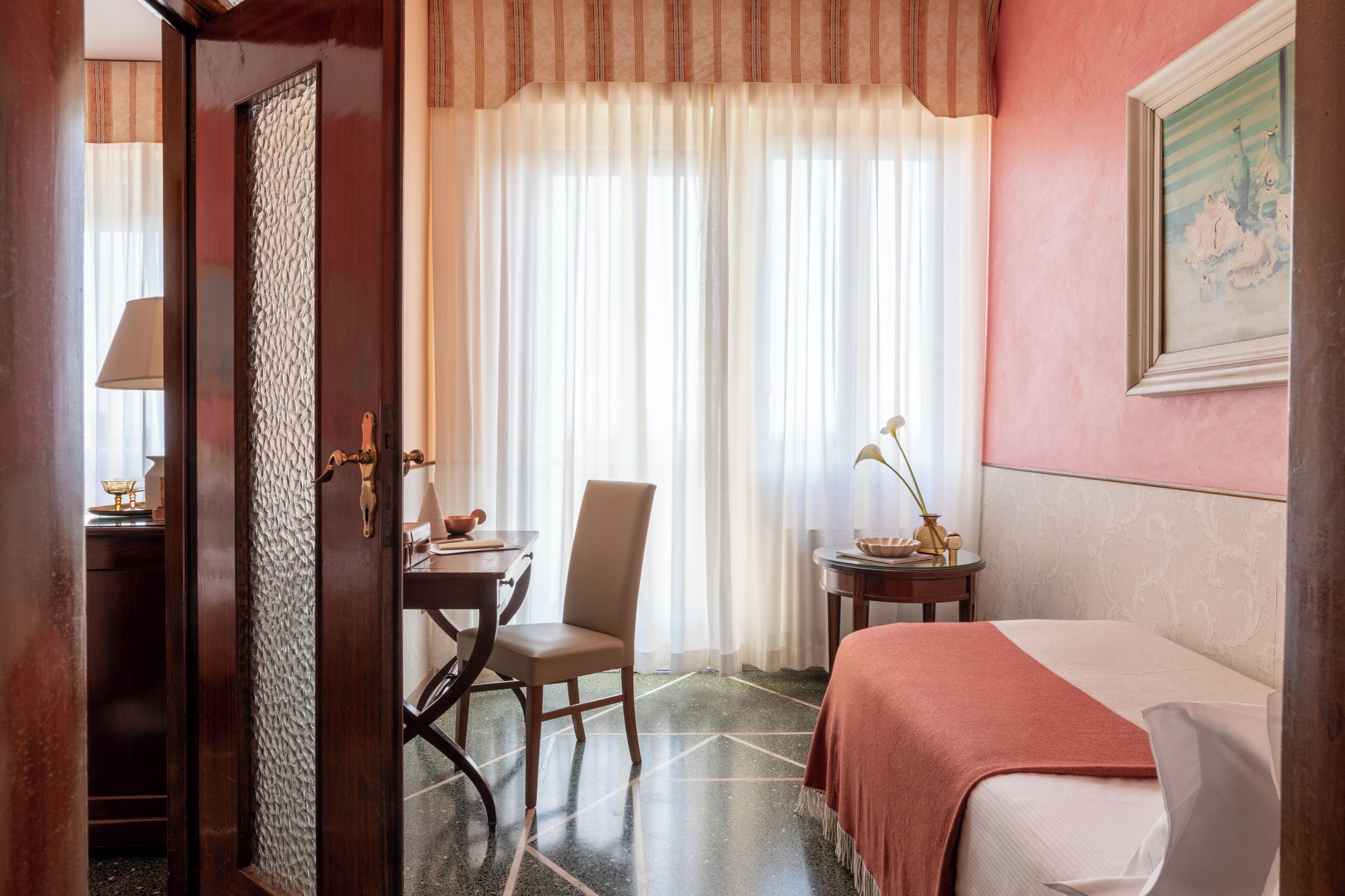 A hotel room with a bed, a chair, a table, and a small table with a lamp.