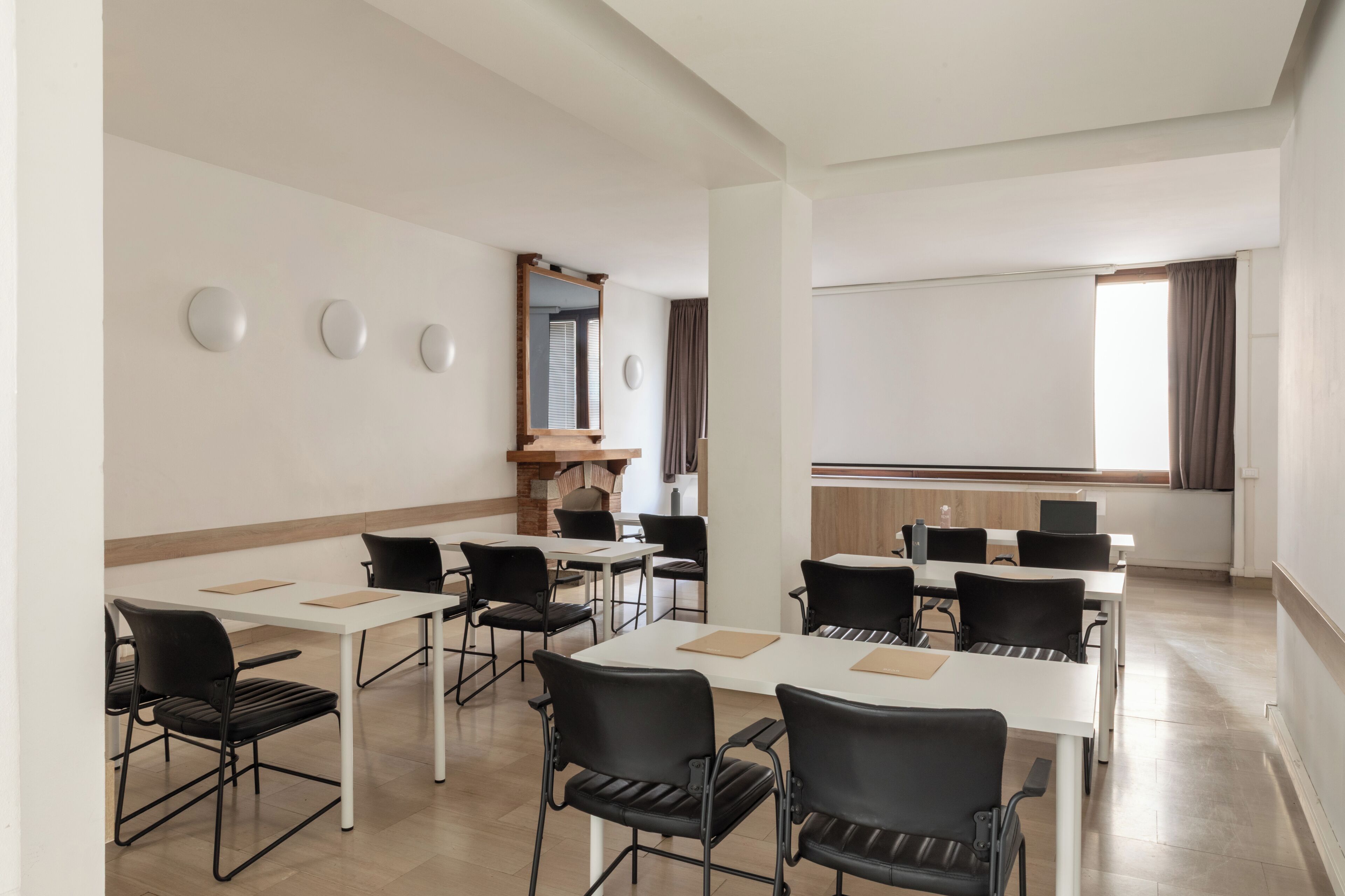 Una sala conferenze con tavoli bianchi, sedie nere, un grande specchio e uno schermo per proiettore.